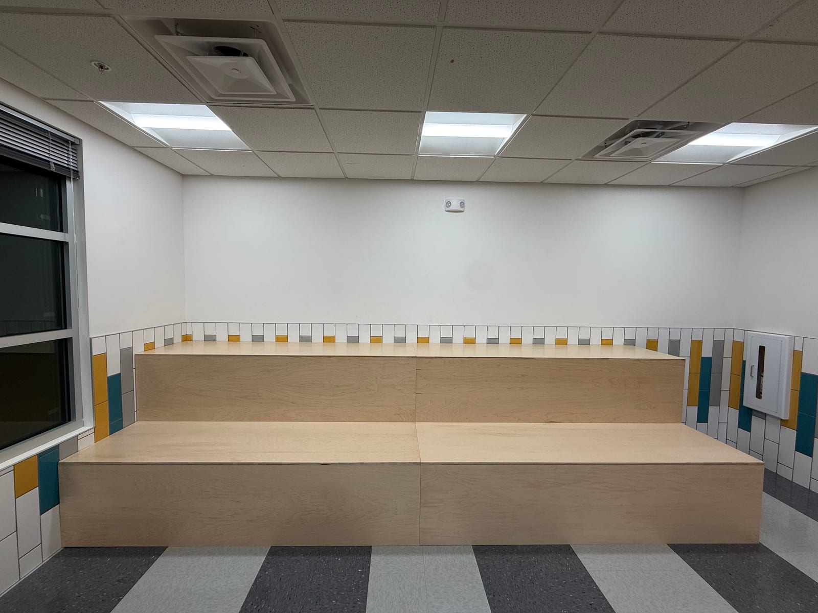 Custom tiered plywood classroom seating built for a private school, clear of the wall-mounted fire-extinguisher cabinet