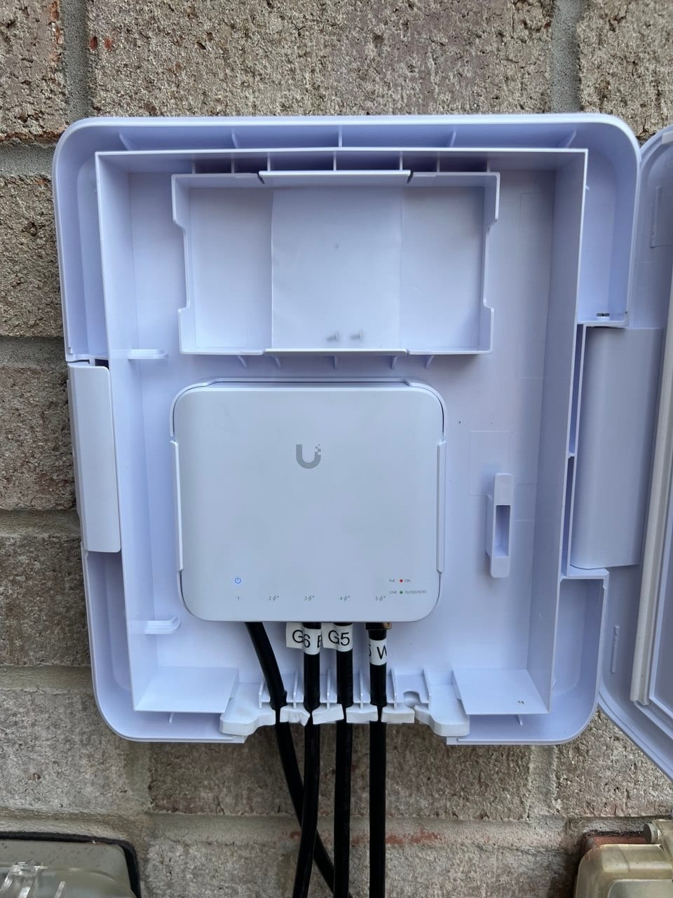 Ubiquiti PoE network switch mounted in a weatherproof outdoor enclosure, with labeled cabling